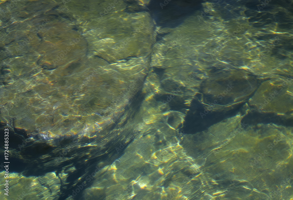 Fototapeta premium Sun-Dappled Riverbed: Reflections and Submerged Stone Textures