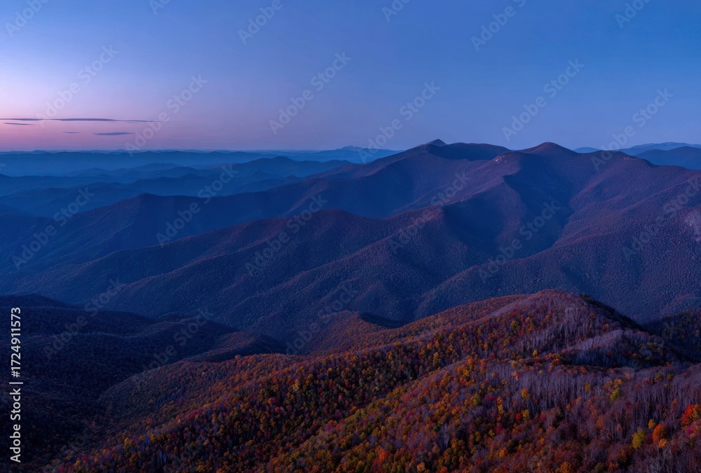 Fototapeta premium A scenic vista reveals rolling mountains layered under a deep blue and pink twilight sky, accented with foliage displaying autumn colors