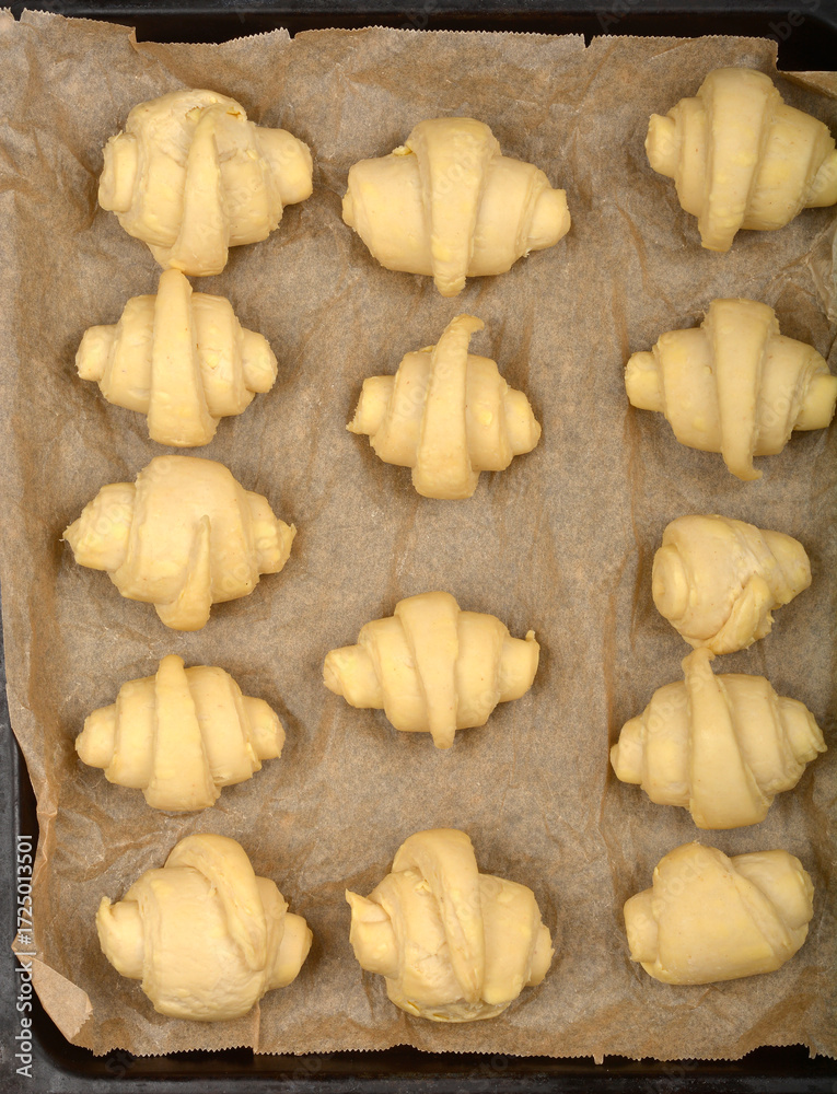 Fototapeta premium An overhead close-up of raw, rolled croissant dough pieces arranged on parchment paper before baking