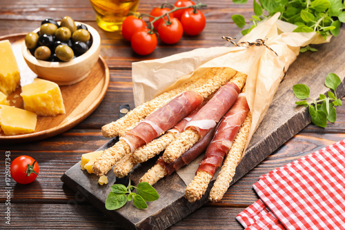 Bild auf Leinwand Grissini breadsticks with prosciutto, cheese, olives and tomatoes on wooden tabl