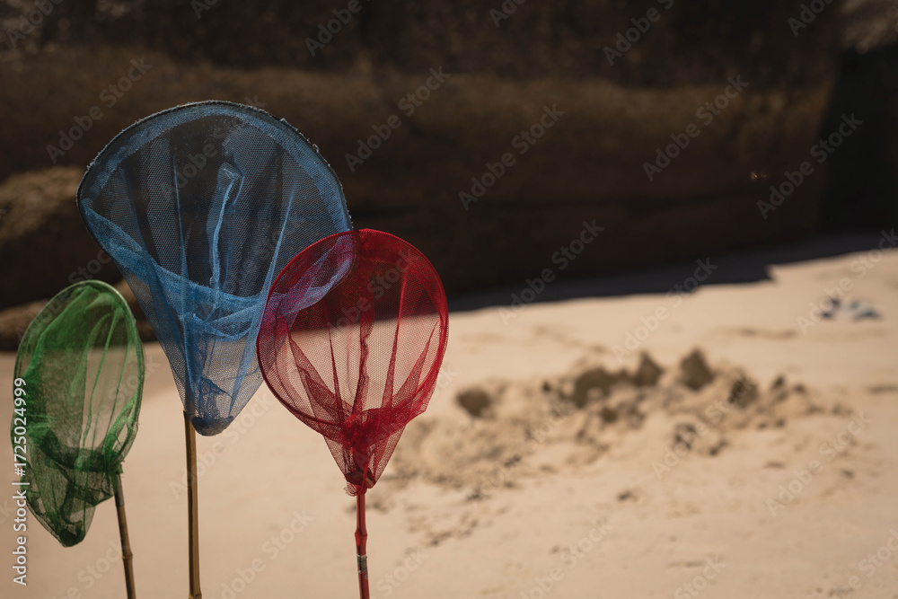 Naklejka premium Three multicolored mesh nets are standing in sand on beach near dark rock and sand pile