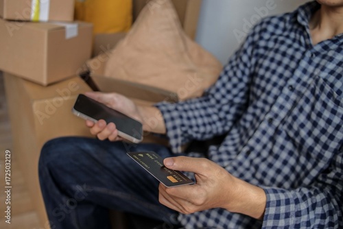 Man Holds Credit Card and Phone Making Payment Amidst Moving Boxes