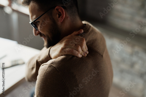 A man holding his shoulder in pain, showing discomfort and tension. The image depicts shoulder pain, muscle strain, or injury
