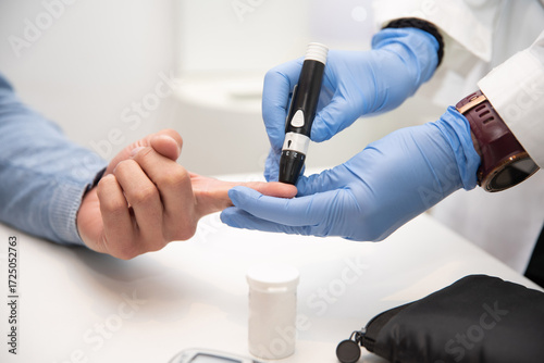 Foto Doctor in blue gloves using a lancing device to prick patient's finger for blood