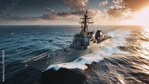 A modern warship cuts through the waves as the sun sets on the horizon. The scene showcases naval strength and the beauty of maritime technology at sea during golden hour