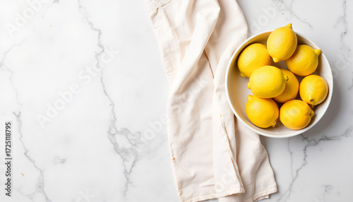 Fresh lemons in white bowl on marble countertop with linen napkin  