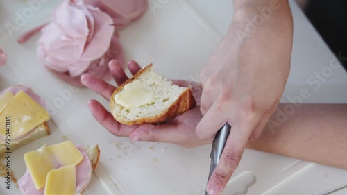 A woman prepares delicious sandwiches with cheese, butter, and sausage in a sunny kitchen. Authentic cooking process showcasing simple, comforting food preparation