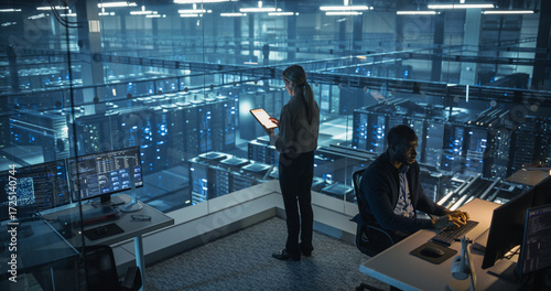Wallpaper Mural Female Cybersecurity Expert Standing with Her Back to Camera, Works on Her Tablet in a Modern Facility, Running Diagnostic Tests to Identify Network Vulnerabilities in a Data Center with Server Racks Torontodigital.ca