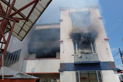 Building burns with thick black smoke billowing from windows, causing damage and concern in the urban area, creating a scene of destruction and urgency.