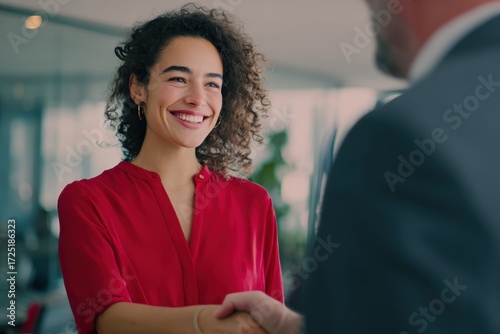 A young, smiling woman in a red shirt shaking hands with a man.