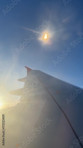 Airplane wing flying above the clouds with sun flare