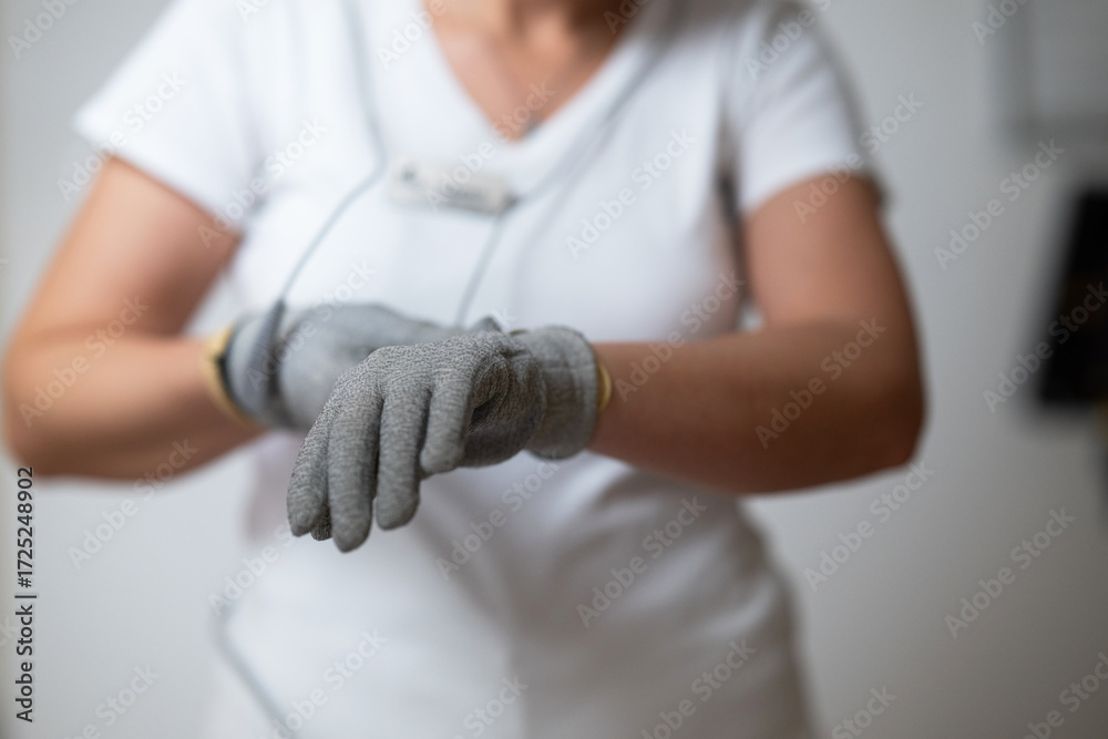 Fototapeta premium Close up shot of a therapist adjusting special conductive electrotherapy gloves before a physiotherapy session. Concept of modern rehabilitation, healthcare technology, pain management, and
