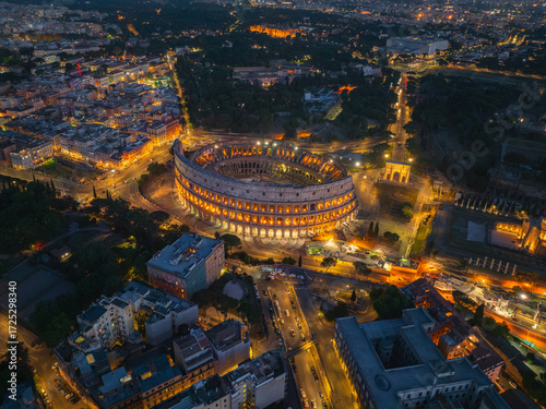 Aerial view of the illuminated Colosseum standing majestically amidst the ancient city's warm glow, a testament to enduring history, Roma, Lazio, Italy.