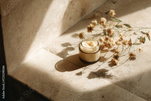 Natural skincare: glass jar of cream and dried flowers in the sunlight on stone steps. Spa aesthetic.