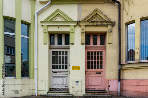Two old wooden doors in townhouse with decorative facades, pastel colors, visible windows and architectural details.