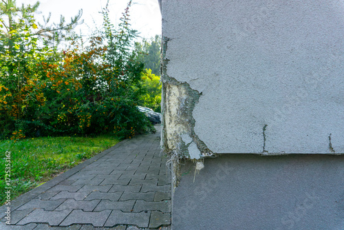 Quadro su tela Close-up of building corner with cracked and peeling facade, exposed reinforcement mesh visible beneath damaged plaster surface