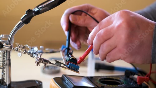 Close-up of hands soldering a printed circuit board with a soldering iron in a workshop. Concept of electronics repair, technology, DIY, and microchip maintenance.