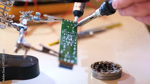 Close-up of hands soldering a printed circuit board with a soldering iron in a workshop. Concept of electronics repair, technology, DIY, and microchip maintenance.