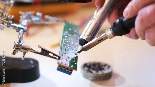 Close-up of hands soldering a printed circuit board with a soldering iron in a workshop. Concept of electronics repair, technology, DIY, and microchip maintenance.