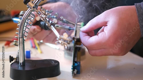 Close-up of hands soldering a printed circuit board with a soldering iron in a workshop. Concept of electronics repair, technology, DIY, and microchip maintenance.
