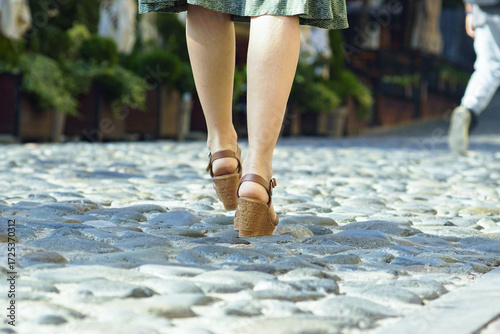Quadro su tela Uncomfortable walk on cobblestone street: woman in wedge sandals struggles with uneven pavement