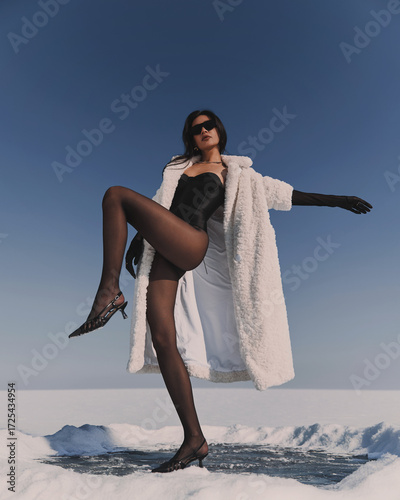 A beautiful and stylish girl in a fur coat walks on a sunny winter day on the frozen sea