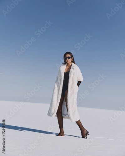 A beautiful and stylish girl in a fur coat walks on a sunny winter day on the frozen sea