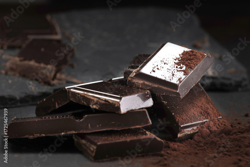 Quadro su tela Broken dark chocolate and cocoa powder on a dark table