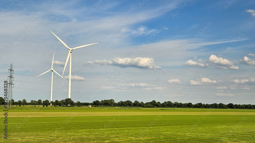 Obraz premium Landscape photo of two tall wind turbines in meadow farming field. Green renewable energy, global warming, climate change, sustainability, farm land concept. 