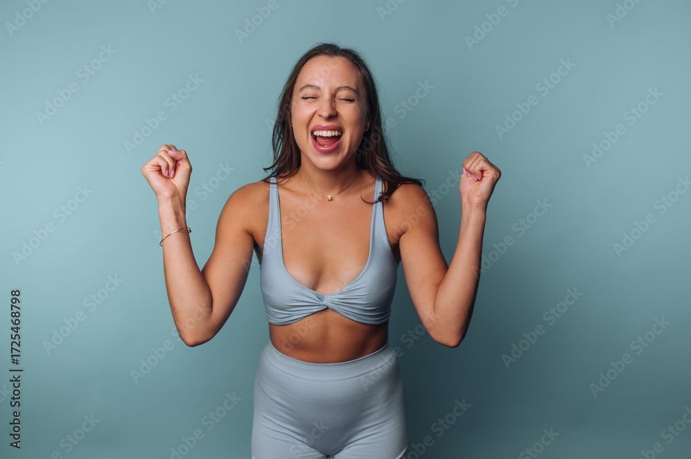Fototapeta premium Woman in activewear celebrating with closed eyes and raised fists.