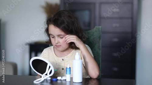 Cute little girl inserting contact lenses into her eye at home. Vision correction and ophthalmology for children