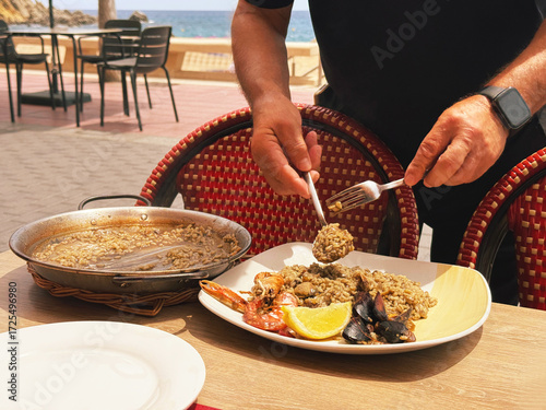 In a spanish restaurant right on the Mediterranean Sea on the Costa Brava, a waiter serves seafood paella. Healthy food on the Mediterranean.