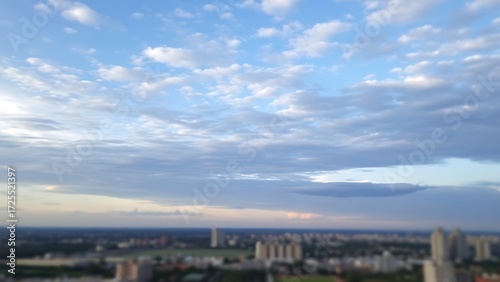 Panoramic sky view with soft clouds, subtly hinting at a blurred cityscape below.