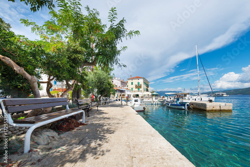 Sitzbank im Schatten unter Bäumen im Hafen von Valun auf der Insel Cres, Kvarner Bucht, Kroatien
