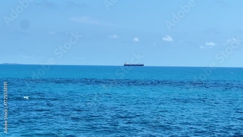 The view of a cargo or tanker ship from afar in the middle of the open blue sea