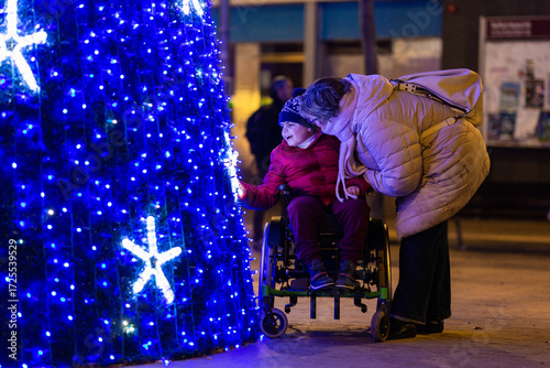 Happy child with disability admiring christmas tree lights with mother at night