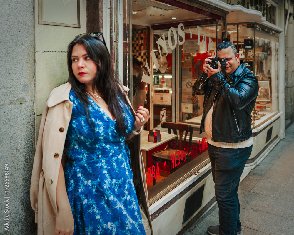 Obraz premium Woman in Blue Dress Leaning Against Wall While Photographer Takes Picture in Madrid Street