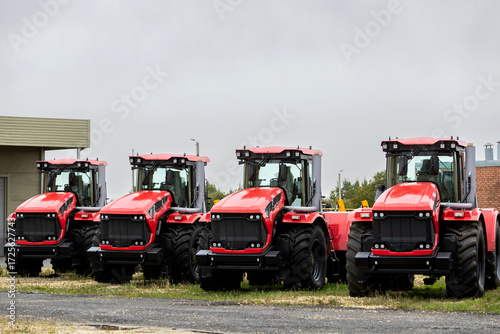 Φωτογραφία Agricultural machinery, four new red tractors, stand in a row in an open parking lot