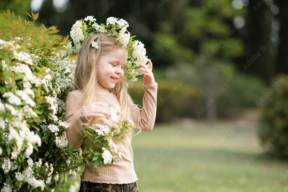 Obraz premium Cute baby girl 3-4 year old wearing floral wreath posing in garden with flowers outdoors. Springtime