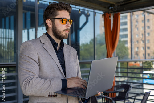 Man in sunglasses typing on a laptop outdoors