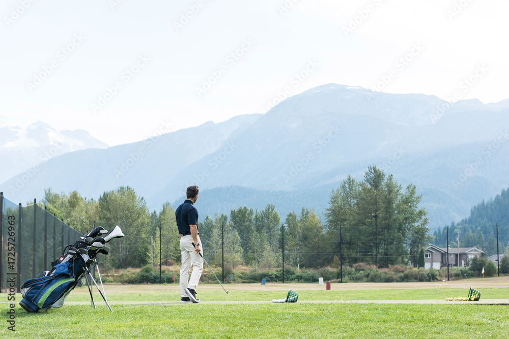 Fototapeta premium Male golfer practicing swing on tee mat at driving range with golf bag, copy space