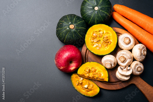 Fresh vegetables and fruits with pumpkin carrot apple and mushrooms on dark background