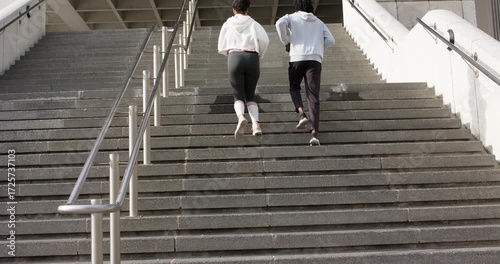 Emerging at bottom of staircase, diverse friends in sportswear running up steps for cardio training