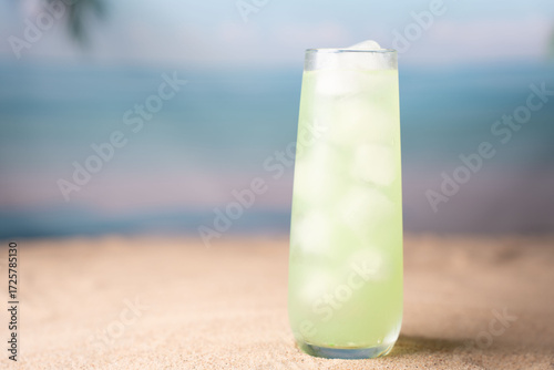 chilled lime green beverage in tall glass on sandy beach with serene ocean and sky backdrop, evoking refreshment and tranquility in a summer paradise setting, scenic, minimalistic, cloudless, waves