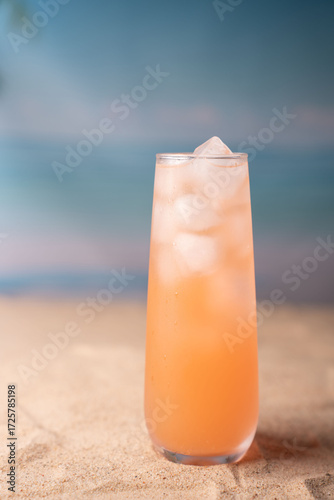 refreshing peach-colored beverage with ice cubes in a tall glass on sandy beach background under a serene blue sky, suggesting a tranquil tropical getaway ambiance, hydrating, soothing, escape