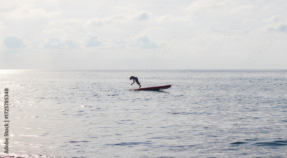 Naklejka premium Young boy dives into the sea from the puddle board. Fun