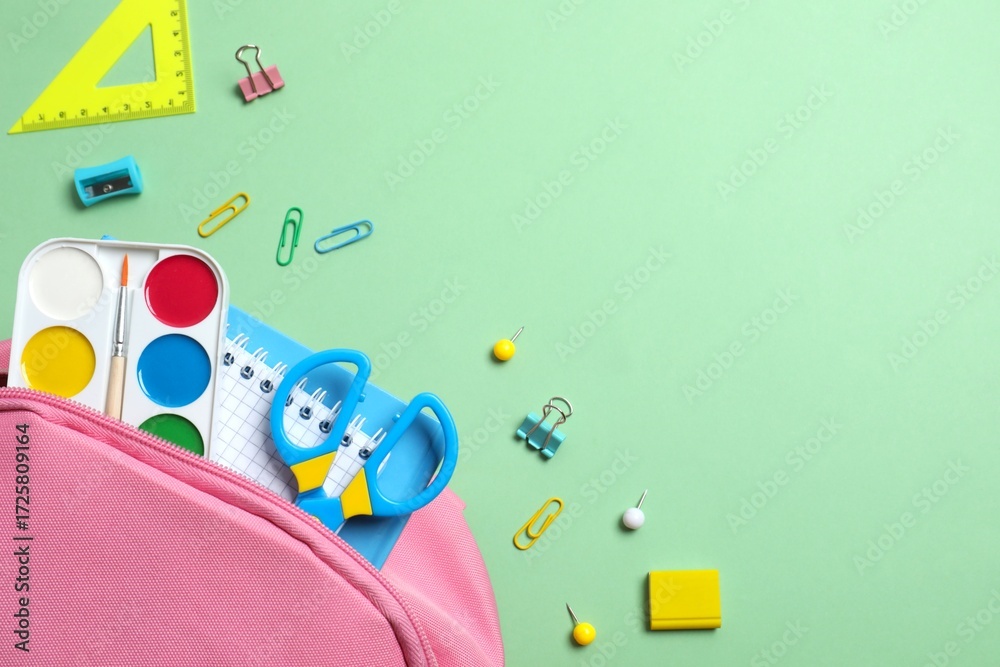 Obraz premium Pink backpack with school supplies on green background. Top view, space for text
