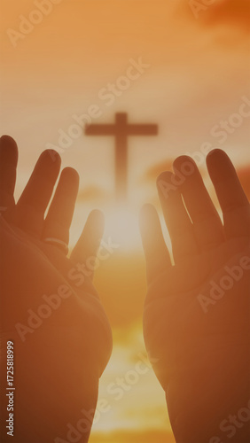  A person's hands are raised in a reverent gesture of prayer or worship, serving as the central focal point. The close-up, balanced composition emphasizes the detailed hands against a softly blurred b