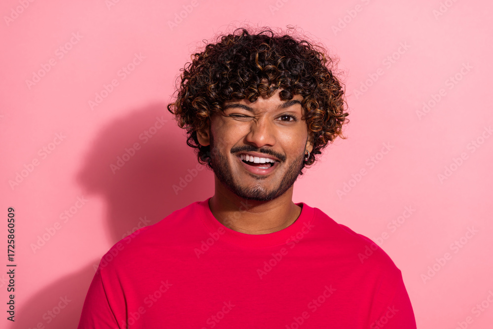 Obraz premium Portrait of a cheerful young man in a red shirt winking confidently against a vibrant pink background
