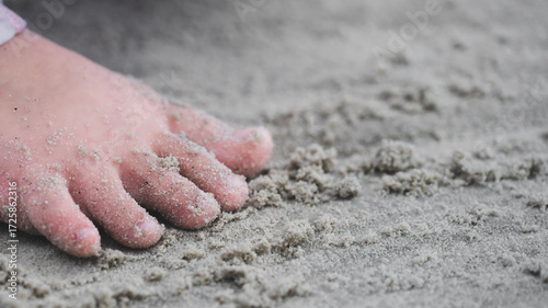 Intimate, detailed close-up of a small child's sandy foot pressing down on fine beach sand. Feeling of being at seaside, childhood freedom, exploration, relaxation, and simple joy of summer a vacation
